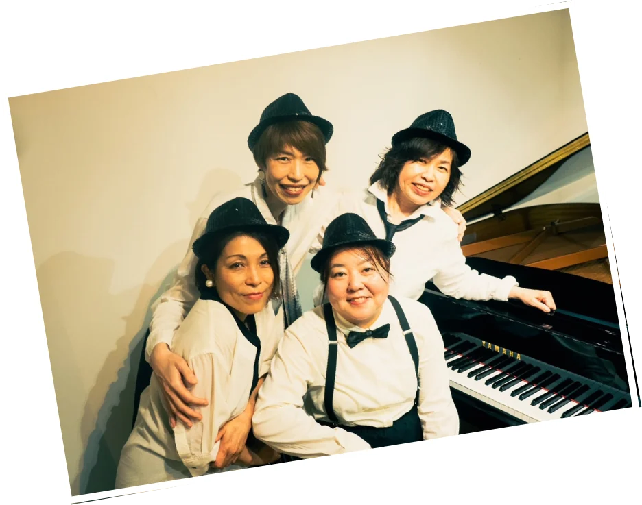 ピアノの前に集まった、帽子姿の凸凹全力中年ママ4人